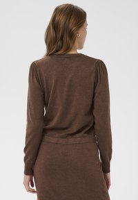 Rjav pleten pulover z dolgimi rokavi in ribastim izrezom, ki ima rahlo naborko na ramah in prilegajoč rob.