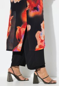 Heldere bloemenpatroon top met rode en oranje tinten, gecombineerd met zwarte cropped broeken en sprankelende zwarte blokhak sandalen.