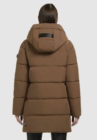 Bruine pufferjack met een gequilt ontwerp, grote capuchon en zwart label op de rug. Heeft een rechte snit en elastische manchetten.