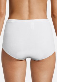 Frau trägt schlichte weiße, hochgeschnittene Baumwollunterwäsche, von hinten vor einem neutralen Hintergrund gezeigt.