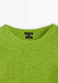Grüner Wollpullover mit rundem Ausschnitt und gerippten Kanten. Sichtbare Etiketten im Inneren, die Größe und Pflegehinweise anzeigen. Weiche Textur.