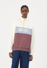 Fél cipzáras pulóver krém, világoskék és mályvaszínű árnyalatokban. A "Converse All-Star" logója, puha tapintása és laza fazonja jellemzi.