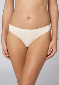 Bikini intimo a vita bassa beige realizzato in tessuto morbido. Presenta un bordo in pizzo e un piccolo fiocchetto al centro anteriore. Design elasticizzato e aderente.