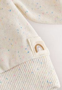 Pull crème clair avec des éclaboussures colorées, ourlet côtelé et un patch en tissu affichant un design d'arc-en-ciel marron.