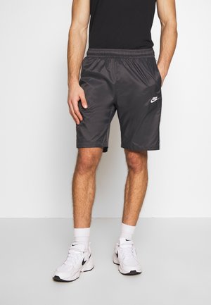 Graue Nike-Shorts mit elastischem Bund und Seitentaschen. Der Stoff hat eine glatte, glänzende Textur und zeigt ein weißes Logo am linken Bein.