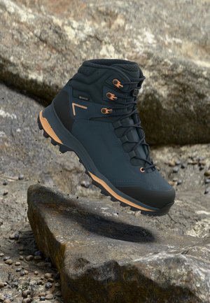 Schwarz-brauner Wanderschuh mit Gore-Tex-Material schwebt über felsigem Gelände, zeigt robuste Sohle und sichere Schnürhaken.