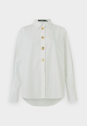 Camicia bianca in cotone a maniche lunghe con colletto classico, chiusura frontale con cinque bottoni dorati e orlo arrotondato. Tessuto morbido con vestibilità su misura.