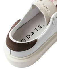 Scarpa da ginnastica bianca con dettaglio in suede marrone sul tallone, tomaia in pelle strutturata e suola spessa bianca. Interno con fodera di colore chiaro e logo del marchio.