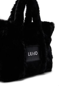 Borsa tote in finta pelliccia nera con due manici in peluche e un'etichetta rettangolare in pelle che mostra il logo "LIU JO". Texture morbida con una forma strutturata.