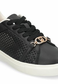 Baskets noires en cuir synthétique avec un panneau en mesh, lacets noirs, détail d écoratif en métal doré et semelle en caoutchouc blanche.