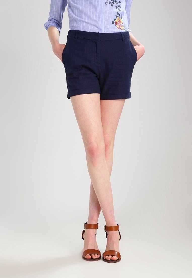 Mörkblå skräddarsydda shorts med fickor, en mjuk textur och uppvikt fåll. Matchas med bruna sandaletter med remmar och bred klack.