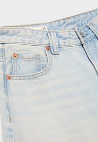 Svetlomodré riflové nohavice - detail predného vrecka, pútka na opasok, kovového gombíka a štítku s veľkosťou „36“.