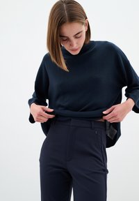 Námořnická modrá oversized pletená svetr s vysokým výstřihem, kombinovaný s dobře padnoucími námořnickými kalhotami s bočními kapsami a hladkou texturou.