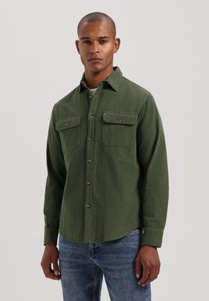 Green button-up shirt made of textured fabric, featuring two chest pockets, long sleeves, and a collar, paired with blue jeans.
