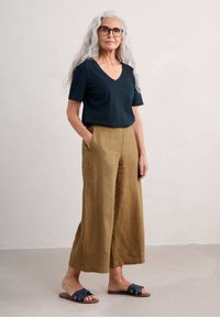 Dark blue v-neck t-shirt, relaxed fit; light brown wide-leg linen pants with pockets; navy blue slide sandals with a braided design.