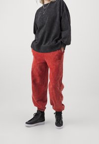 Schwarzes, übergroßes Sweatshirt mit einer verblassten Textur, kombiniert mit lockeren roten Jogginghosen mit einer Seitenk Tasche und schwarzen High-Top-Sneakern.