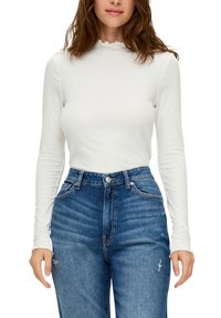 Bílý žebrovaný dlouhý rukáv top s vlnitým výstřihem, zkombinovaný s modrými vysokými džínami s odřeninami.