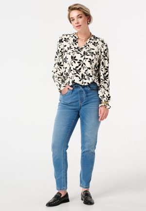Chemisier à manches longues avec un motif de feuilles noires sur fond crème, accompagné de jeans taille haute bleu clair et de mocassins noirs à clous.