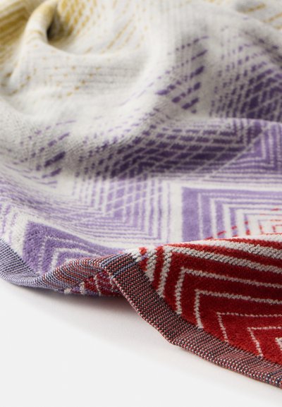 Tissu tissé doux avec des motifs géométriques en zigzag dans des tons violet, rouge et jaune, présenté sur une surface blanche.