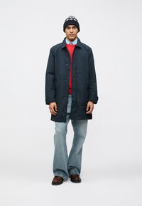 Námornícky modrý kabát strednej dĺžky so západkami, nosený cez červený sveter a rozšírené džínsy. Pridaný vzorovaný čiapka. Hnedé topánky.