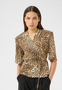 Leopard print wrap blouse in beige and black, made from smooth fabric. Features short sleeves, a v-neckline, and a tie waist detail.
