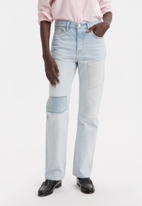 Svetlo modré džíny z denimu s vysokým pásom, s viacerými nášivkami v rôznych odtieňoch modrej, s rovnými nohavicami a rozstrapkanými okrajmi.