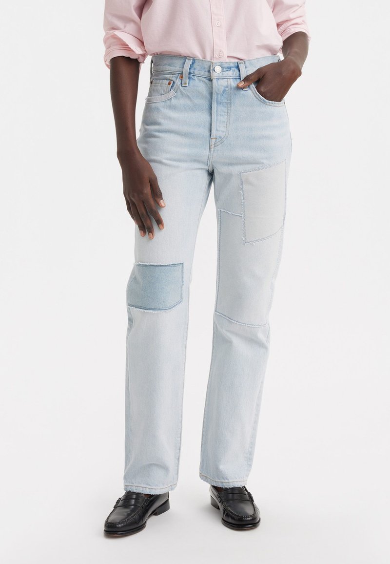 Jeans in denim azzurro chiaro con vita alta, dotati di numerosi toppe in diverse tonalità di blu, taglio dritto e orli sfilacciati.