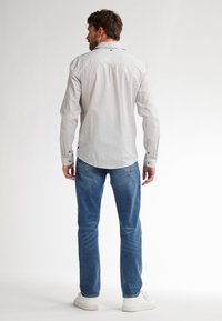 Camicia a righe con maniche lunghe in bianco sporco e blu navy, con colletto a punta e polsini con bottoni, abbinata a jeans in denim blu e sneakers bianche.