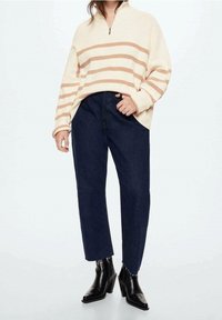 Pull crème avec des rayures rouille, col zippé à mi-hauteur ; associé à un jean foncé taille haute et des bottines noires à talon �épais.