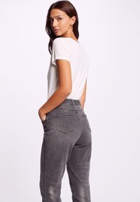 T-shirt bianca a maniche corte abbinata a pantaloni in denim grigio a vita alta con tasche posteriori e una leggera texture sbiadita.