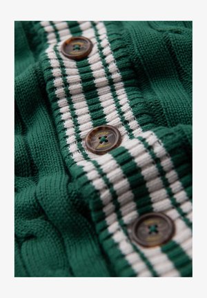 Tissu tricoté vert avec des rayures blanches. Quatre boutons marron avec un motif croisé et un texte en relief près du centre. Motif texturé visible.