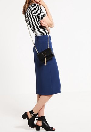 Top a righe a maniche corte, gonna blu fino al ginocchio, borsa a tracolla nera con nappina e sandali neri con tacco e cinturino alla caviglia.