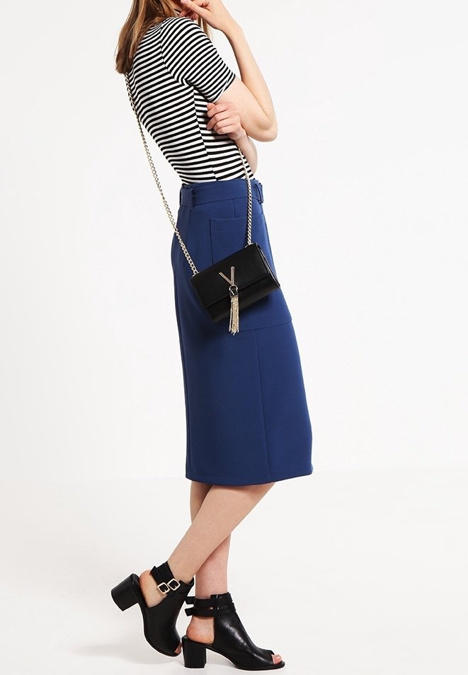 Randig kortärmad topp, blå knä-lång kjol, svart axelväska med fransar och svarta klacksandaler med ankelremmar.