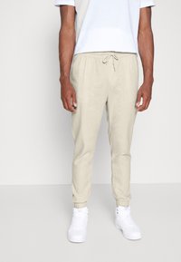 Ljust beige joggerbyxor med elastiska muddar och midja, detaljer med dragsko, tillverkade av ett lätt material, kombinerade med vita sneakers.