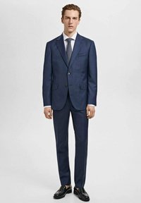 Marineblåt jakkesæt lavet af fint stof med en to-knapsjakke, skrå klapper og slim-fit bukser. Kombineret med en lys skjorte og slips.