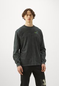 Long-sleeve, dark gray shirt made of soft cotton, featuring a green Nike logo on the chest and a relaxed fit with ribbed cuffs.