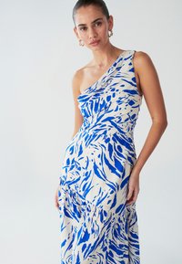 Robe asymétrique avec une épaule dégagée, affichant un motif abstrait bleu et blanc, confectionnée dans un tissu doux avec une silhouette fluide et des détails froncés à la taille.