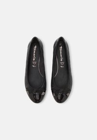 Bailarinas negras con una puntera de charol brillante, textura acolchada en los lados y un acento de lazo con detalles metálicos.