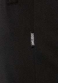 Zwarte sportbroek met een gladde textuur, voorzien van zijzakken en een klein wit logo label voor merkidentificatie.