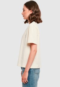 Kortærmet cremefarvet bomulds T-shirt med en løs pasform, der har minimal broderi på venstre side. Glat tekstur med rund halsudskæring.