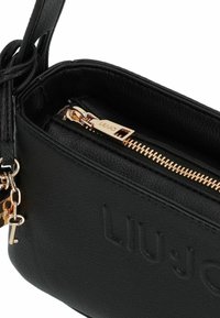 Bolso de mano de cuero negro con textura, con el logo "LIU JO" en relieve, cremallera dorada y llaveros dorados en forma de llave sujetos a la correa.