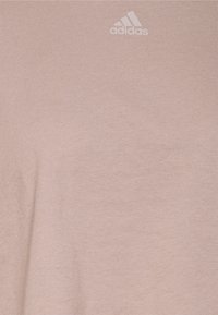 Ljusrosa bomulls-t-shirt med en mjuk textur och subtil randedesign. Har en liten vit Adidas-logotyp i det övre vänstra hörnet.