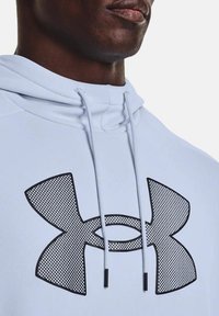 Hoodie bleu clair avec un grand logo en texture maillée noire au centre. Des cordons blancs avec des embouts noirs complètent le design.