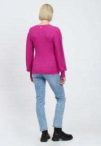Stram pink ribstrikket sweater med lange ærmer, høj hals og teksturerede detaljer. Kombineret med lyseblå denim og sorte ankelstøvler.