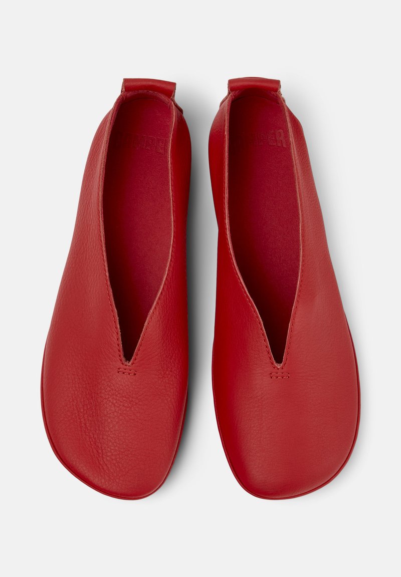 Red, flat slip-on shoes with a smooth leather finish and a v-shaped cutout at the front, displayed on a neutral background.