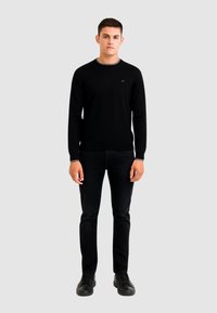 Zwarte gebreide trui met ronde hals, gecombineerd met zwarte broek en zwarte sneakers. Eenvoudig ontwerp, slim fit, geen zichtbare patronen.