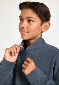 Grå fleece-pullover med hög krage och halvdragkedja. Har långa ärmar och en mjuk textur för värme och komfort.