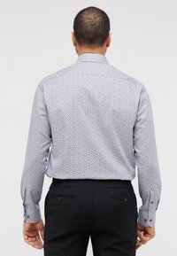 Langarmhemd in helllila mit kleinem Blättermuster, ausgestattet mit einem klassischen Kragen und geknöpften Manschetten, getragen zu schwarzen Hosen.