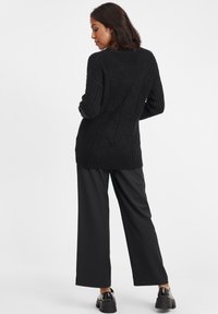 Maglione nero lavorato a maglia con un motivo testurizzato, caratterizzato da maniche lunghe e una vestibilità leggermente oversize, abbinato a pantaloni neri a gamba larga e scarpe chunky.