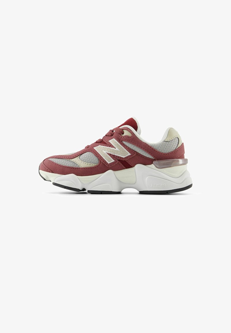 Zapatilla deportiva en rojo y gris con parte superior de malla y ante, entresuela blanca, suela negra y prominente logotipo 'N' en el lateral.